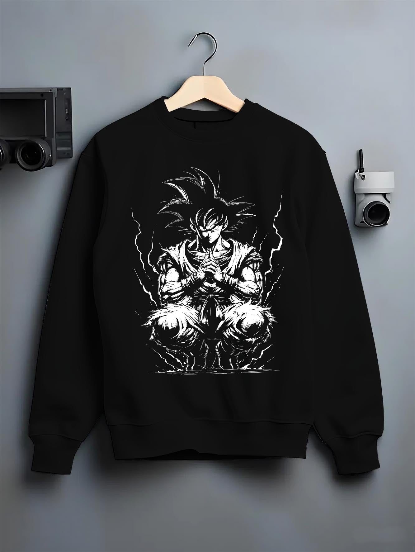 Black crewneck sweatshirt on a hanger against a grey wall, featuring Dragon Ball Goku retro manga graphic meditation pose with aura energy in anime poster inspired design.
