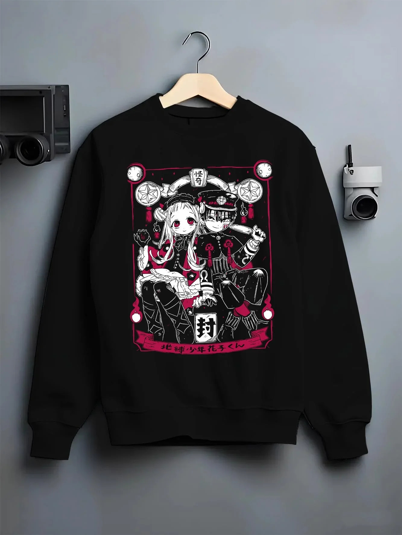 Black crewneck sweatshirt on hanger against grey wall, featuring cult classic anime poster inspired Hanako-kun and Nene Yashiro retro streetwear graphic.